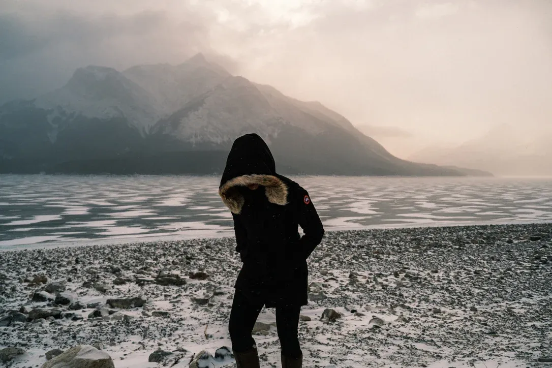 Person in dark clothing standing near a cold mountain lake