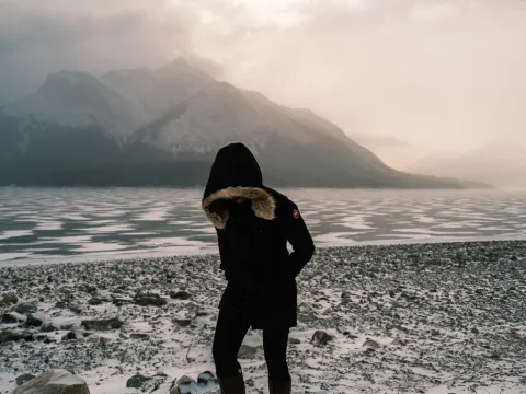 Person in dark clothing standing near a cold mountain lake