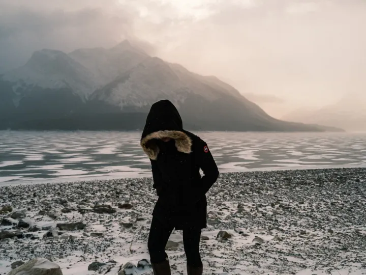 Person in dark clothing standing near a cold mountain lake