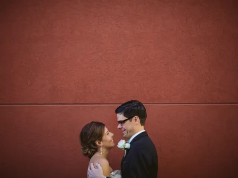 Bride and groom smiling at each other beneath a large terracotta textured wall