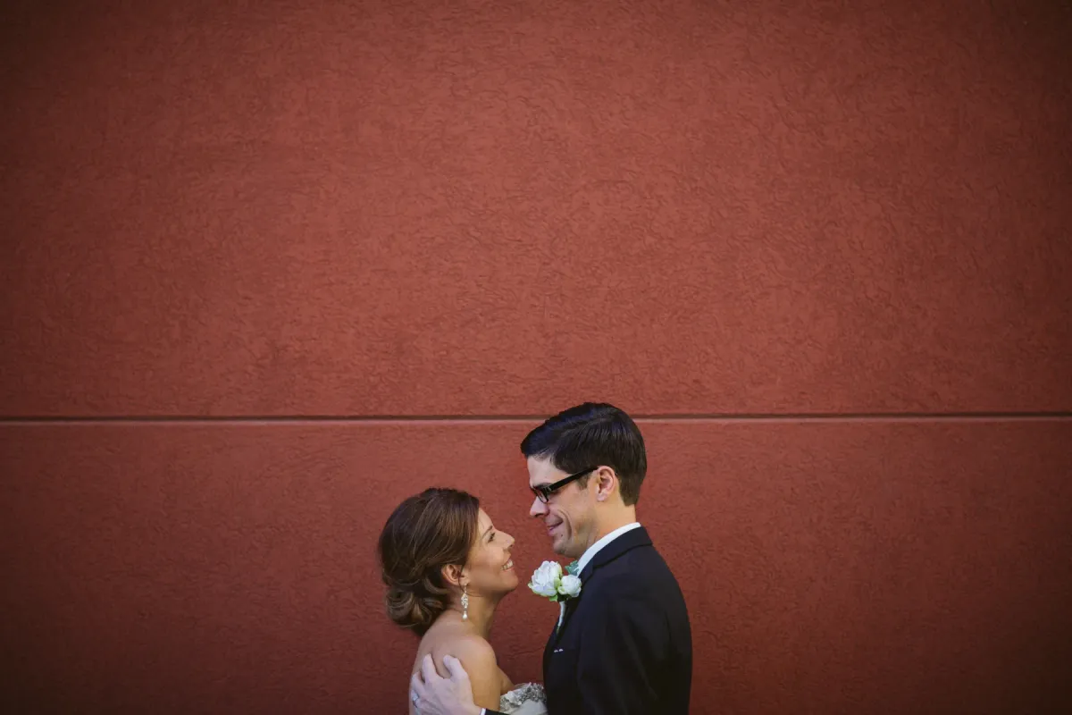 Bride and groom smiling at each other beneath a large terracotta textured wall