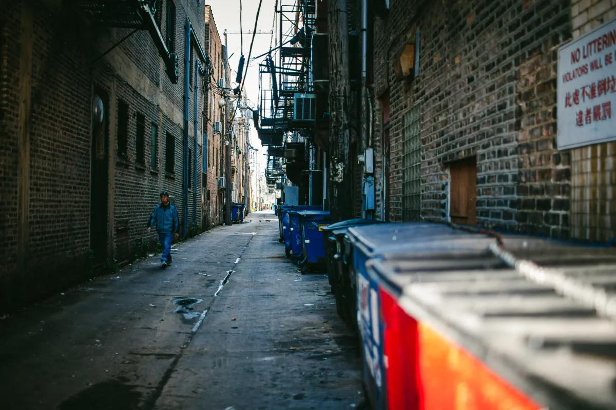 Narrow brick alley with blue shadows and bins along the wall