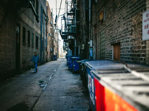 Narrow brick alley with blue shadows and bins along the wall