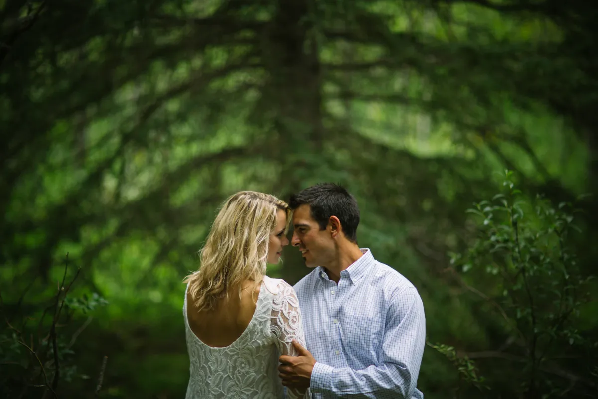 Engaged couple leaning close for an almost kiss in evergreen trees