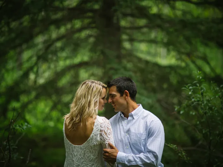 Engaged couple leaning close for an almost kiss in evergreen trees