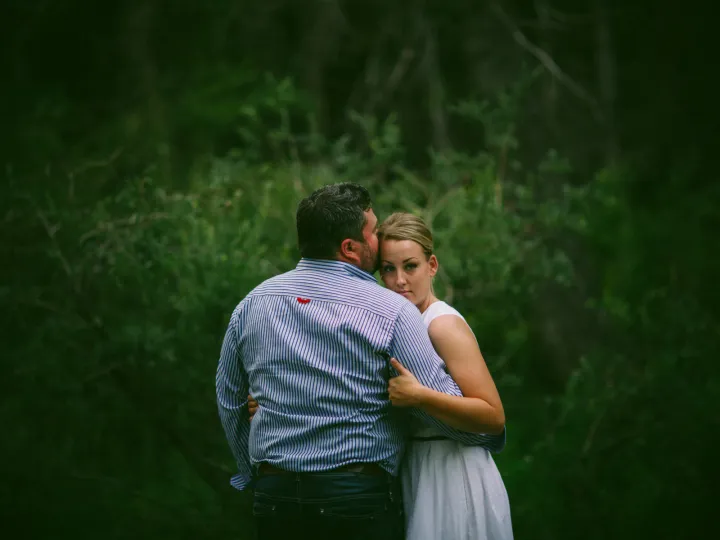 Couple sitting close in the woods with an arm around her shoulders