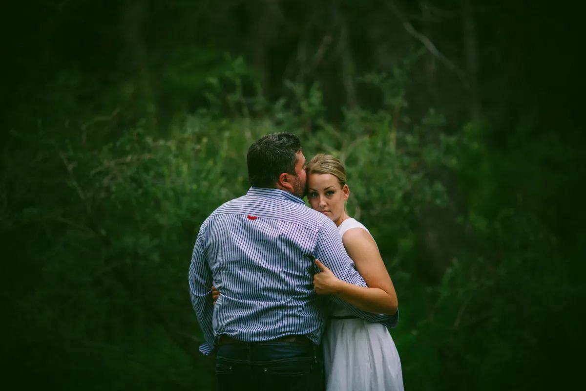 Couple sitting close in the woods with an arm around her shoulders