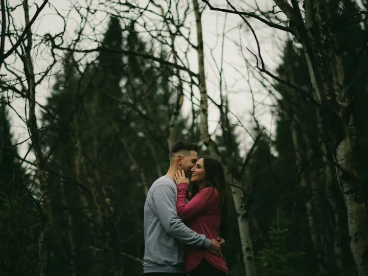 Couple kissing in a dark stand of bare trees during an engagement session