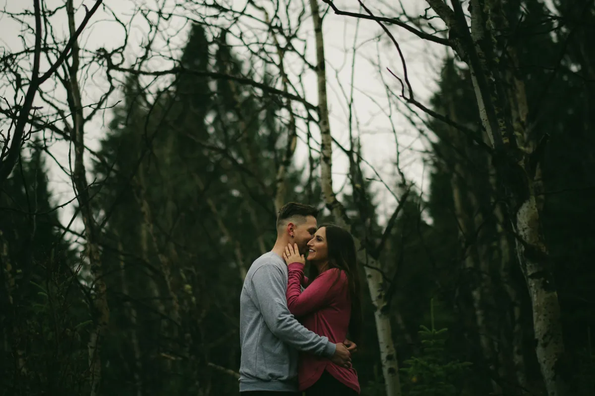 Couple kissing in a dark stand of bare trees during an engagement session