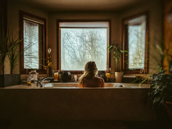 Person sitting in a bathtub beneath warm window light in a rustic room