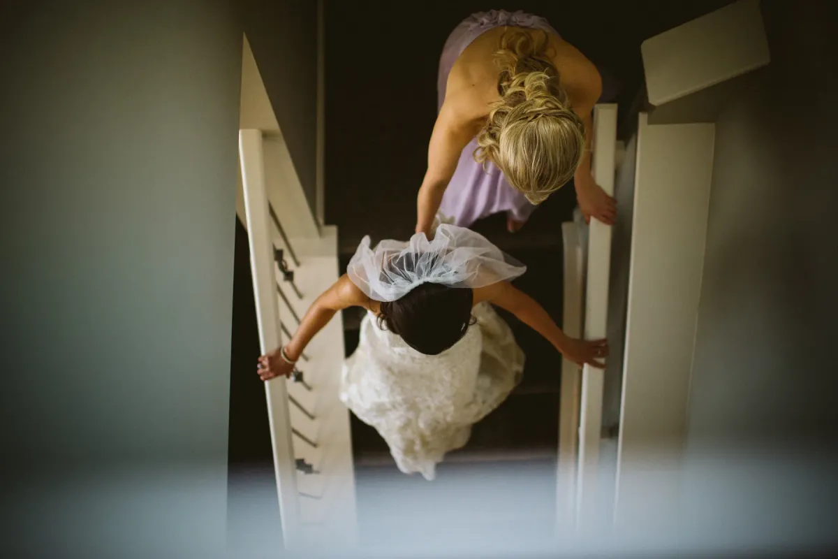 Overhead view of a bride in lace and a lilac bridesmaid descending a carpeted staircase