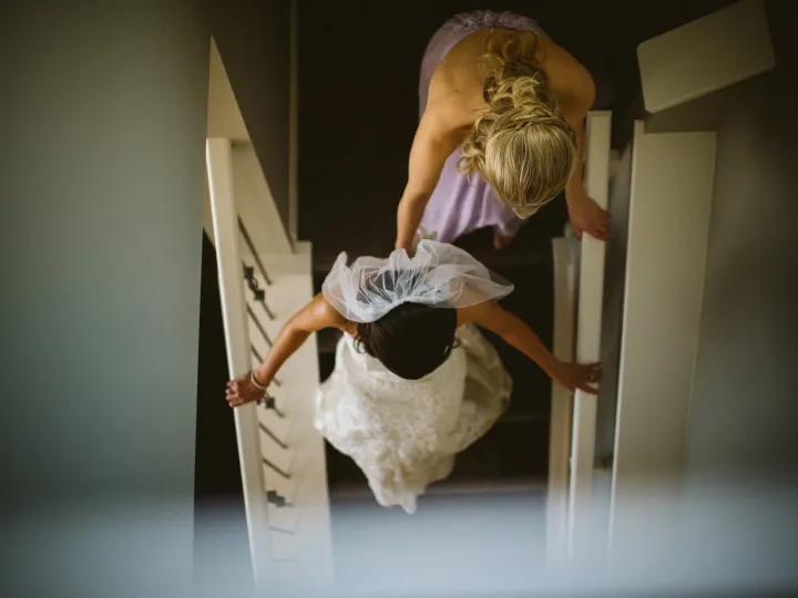 Overhead view of a bride in lace and a lilac bridesmaid descending a carpeted staircase