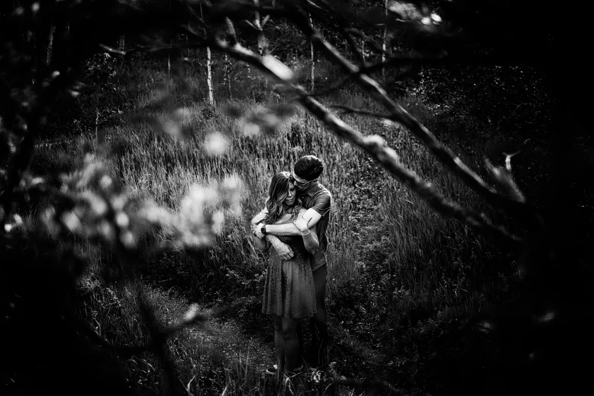 Black and white forest portrait of a couple sitting close during an engagement session