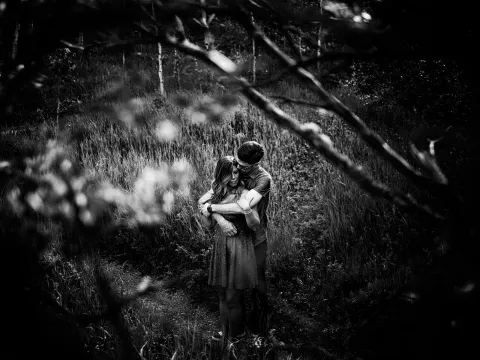 Black and white forest portrait of a couple sitting close during an engagement session