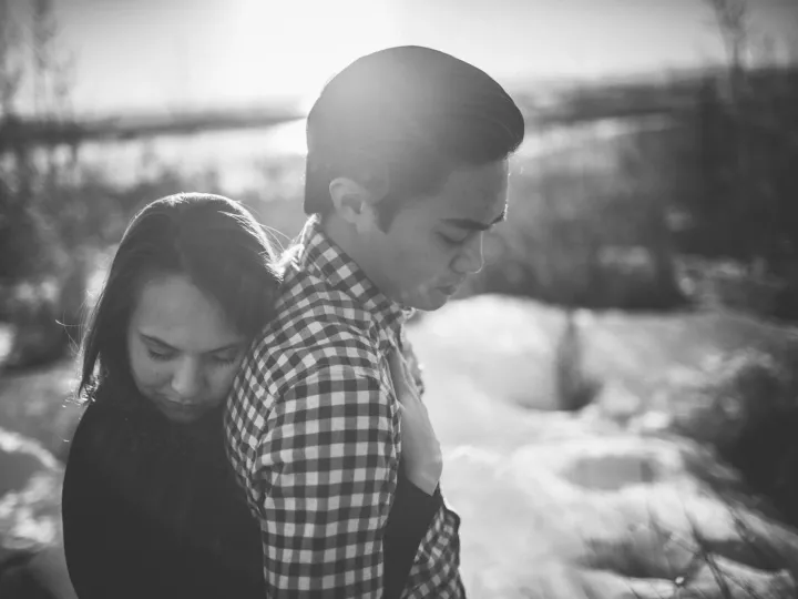 Black and white engagement portrait of a couple standing close in winter trees