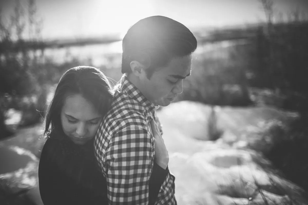 Black and white engagement portrait of a couple standing close in winter trees