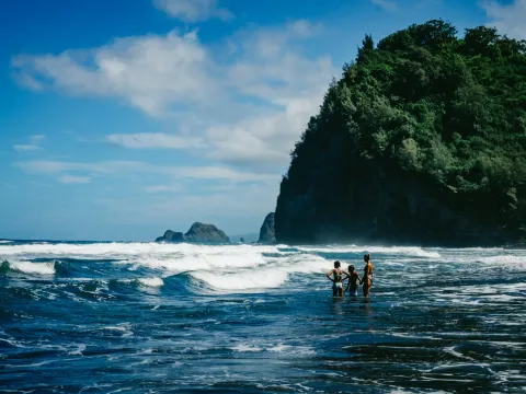 People standing in bright blue water near a black sand beach in Hawaii