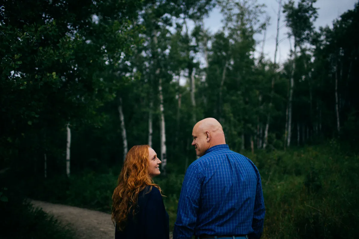 Couple facing each other in a green forest during an engagement session