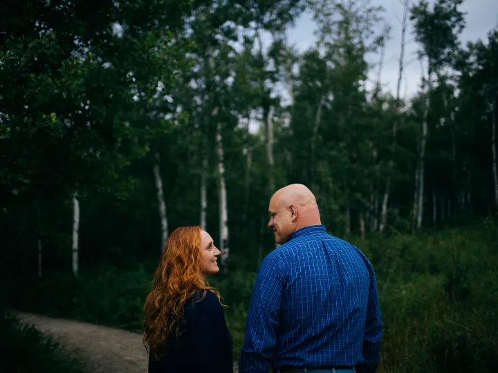 Couple facing each other in a green forest during an engagement session