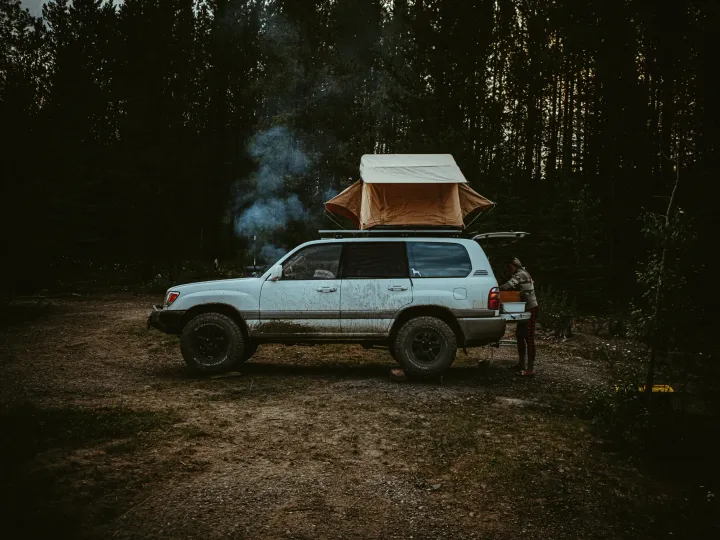 White truck at a forest camp with smoke rising in warm evening light