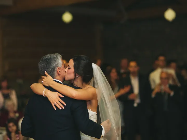 Bride kissing her father's cheek during a reception dance in a wooden lodge