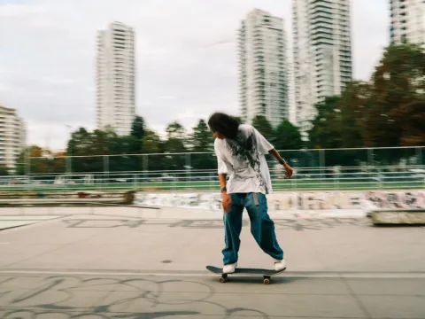 Skateboarder moving across an urban concrete space with tall buildings behind