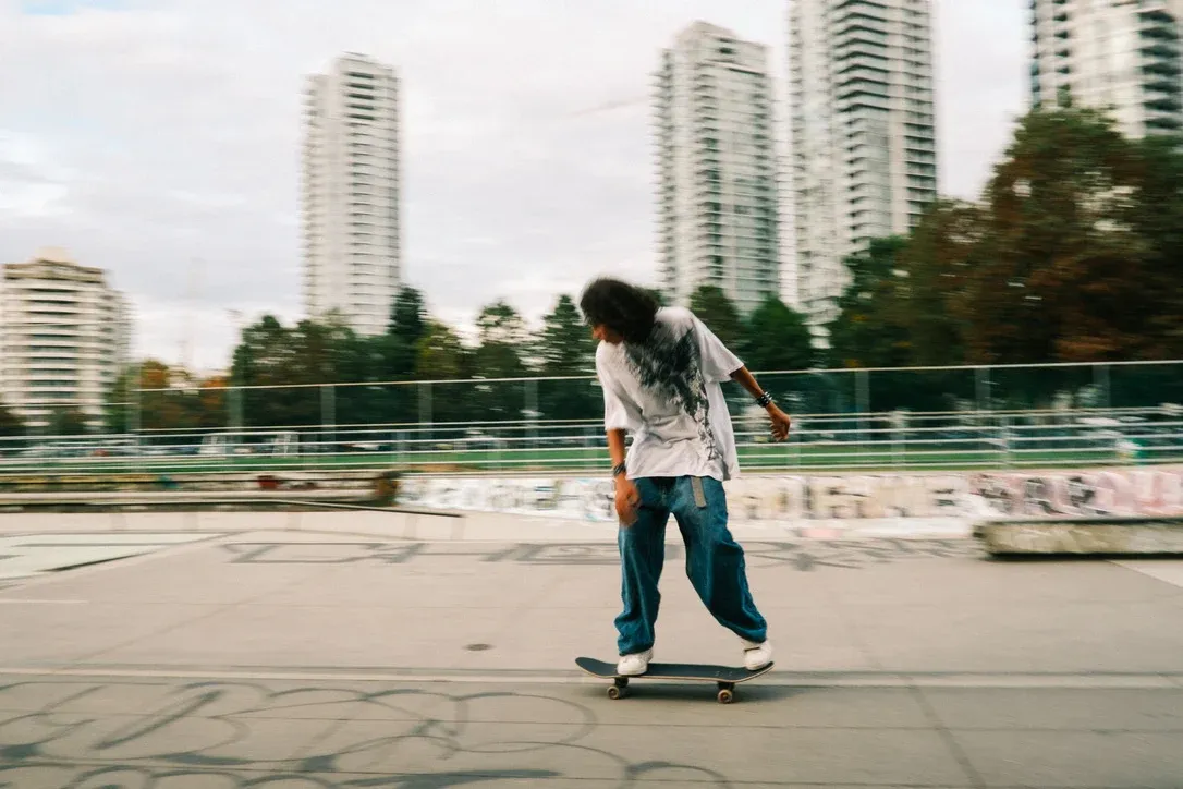 Skateboarder moving across an urban concrete space with tall buildings behind