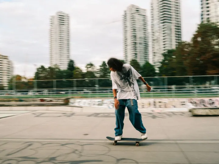 Skateboarder moving across an urban concrete space with tall buildings behind