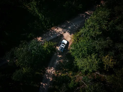 Aerial view of a Land Cruiser moving through a dirt road surrounded by green trees