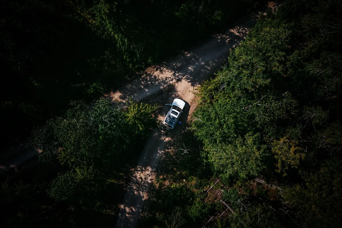 Aerial view of a Land Cruiser moving through a dirt road surrounded by green trees