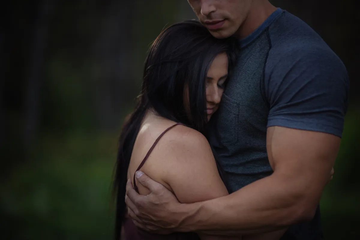 Couple holding close in a dark green outdoor engagement portrait