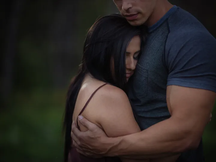Couple holding close in a dark green outdoor engagement portrait