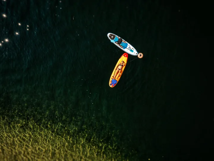 Overhead view of a girl lying on a paddle board in dark lake water