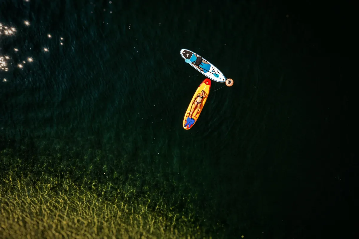 Overhead view of a girl lying on a paddle board in dark lake water