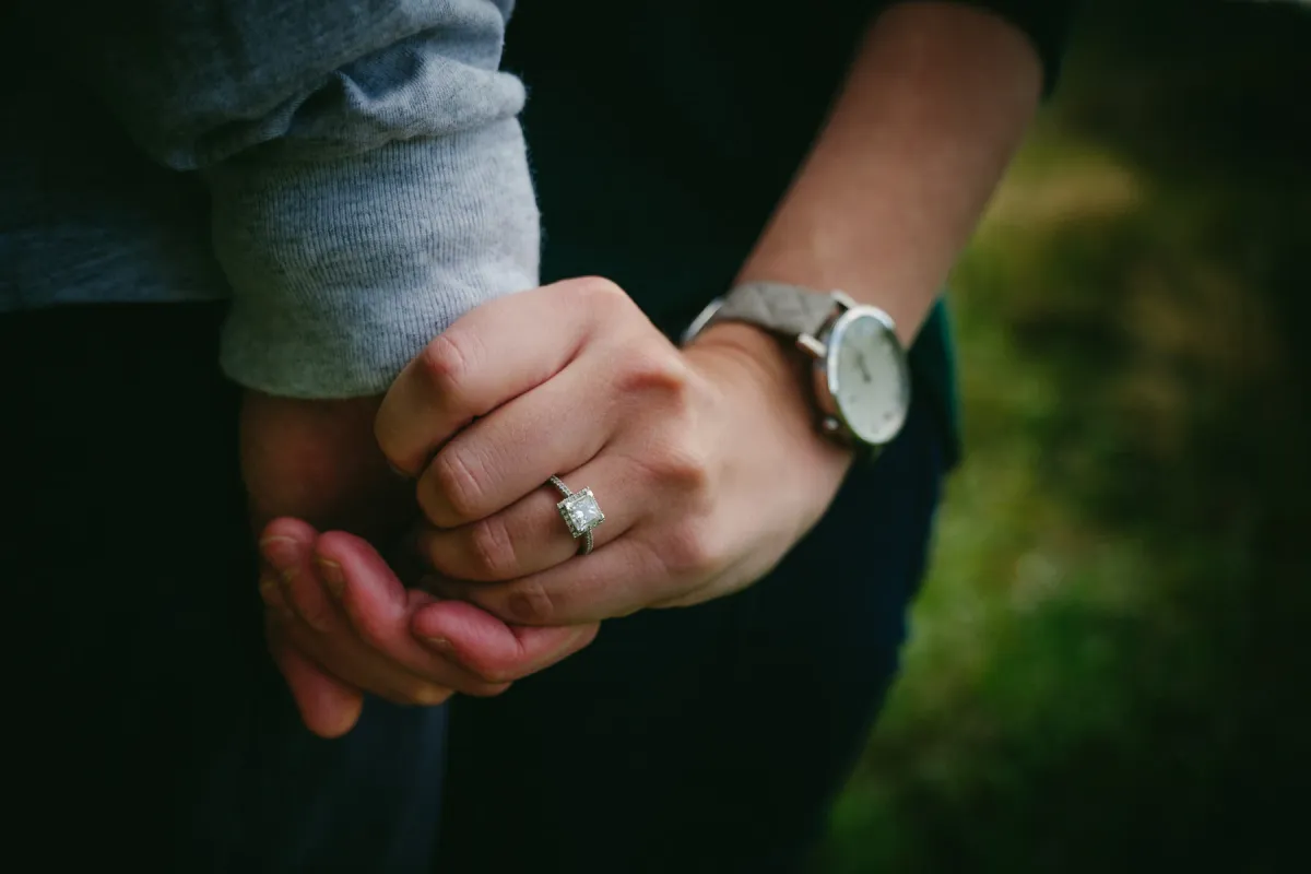 Close photo of a couple holding hands with an engagement ring visible