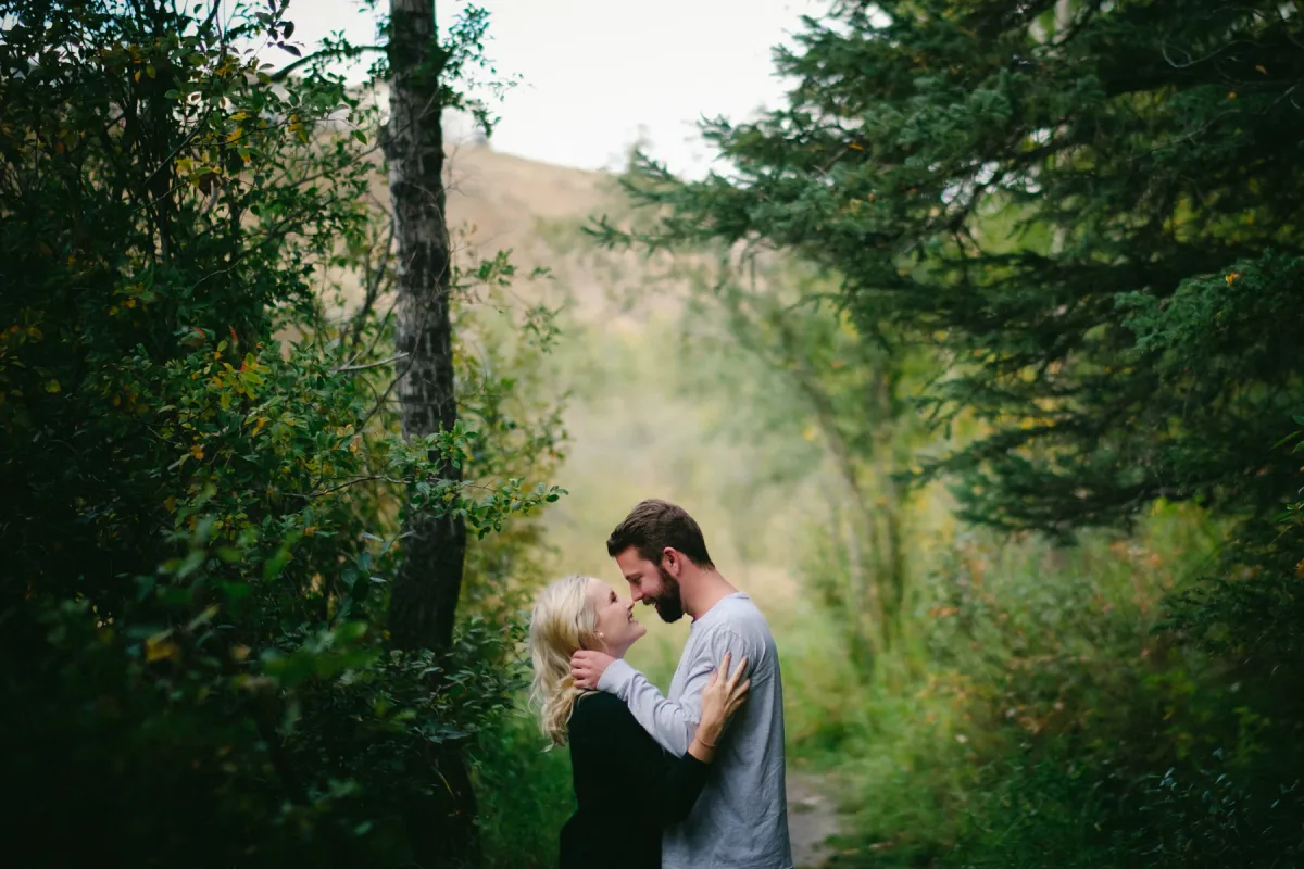 Couple kissing among green forest trees during an Alberta engagement session