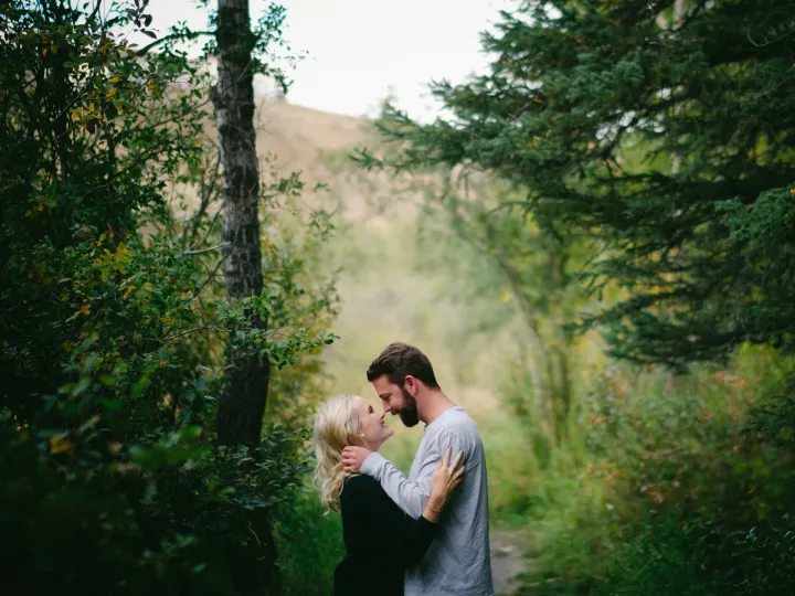 Couple kissing among green forest trees during an Alberta engagement session