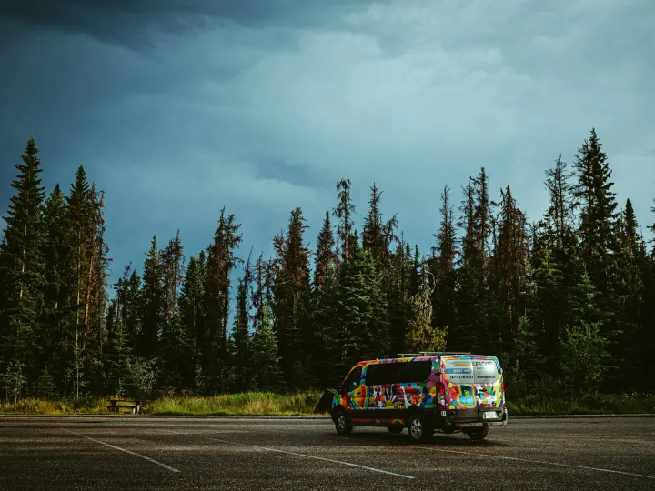 Bright party van with free hugs painted on it parked in an empty lot beneath storm clouds