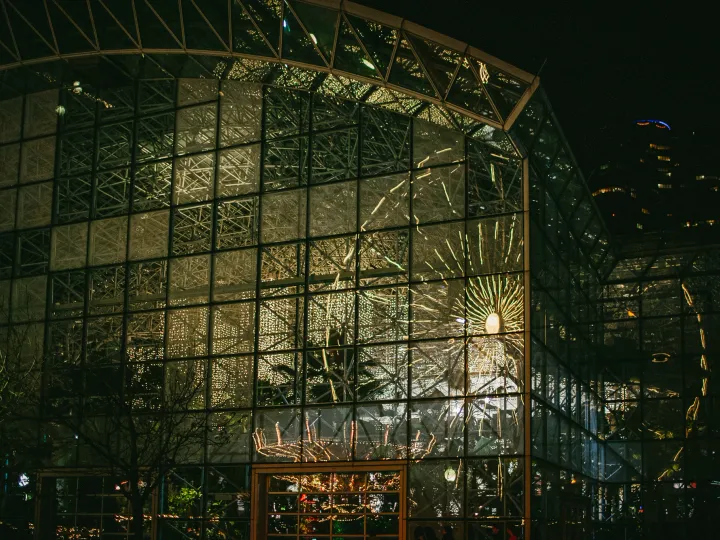 Large glass building glowing at night with people visible inside