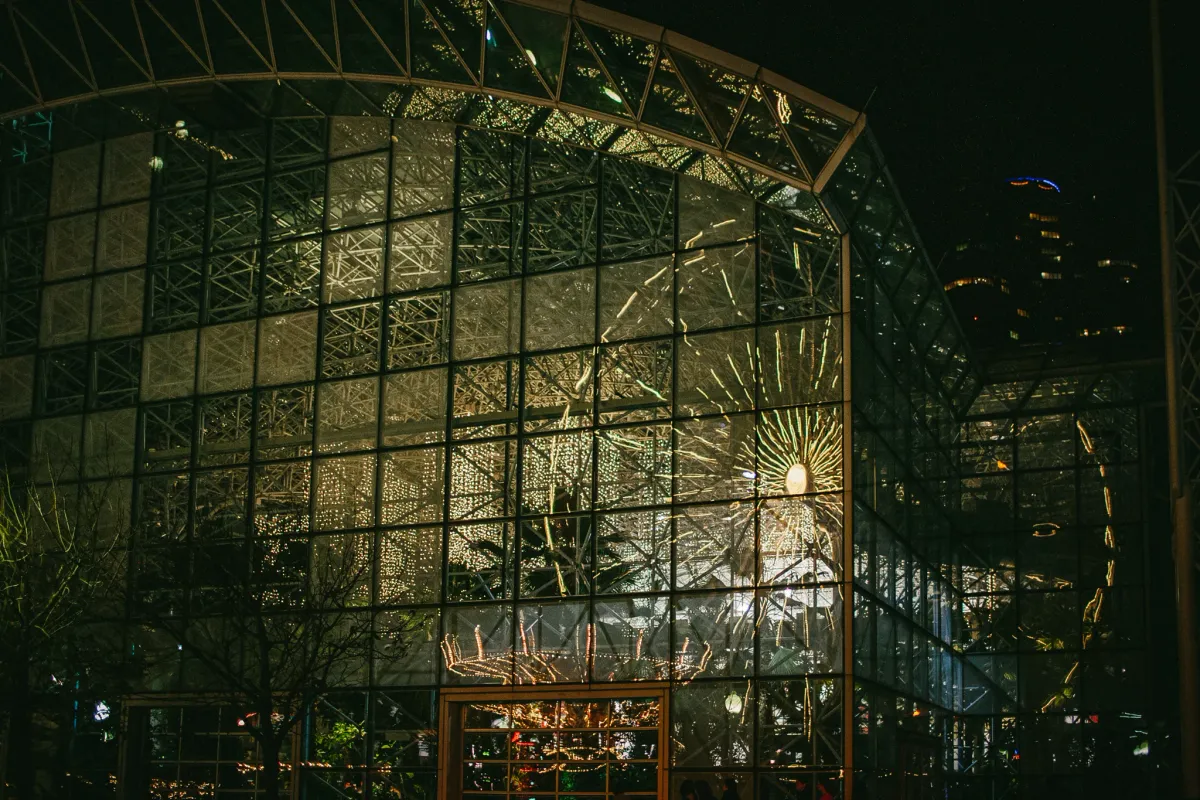 Large glass building glowing at night with people visible inside