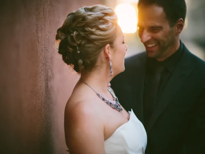 Bride and groom laughing in golden hour light beside a terracotta stucco wall