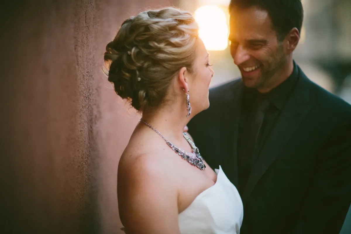 Bride and groom laughing in golden hour light beside a terracotta stucco wall