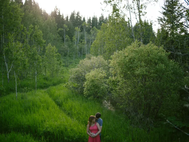 Small couple standing in a green valley during an Alberta engagement session