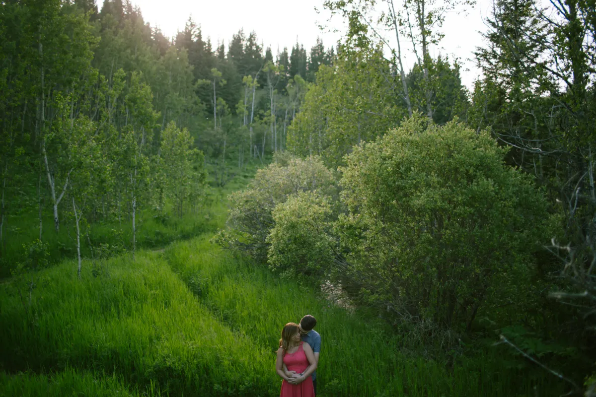 Small couple standing in a green valley during an Alberta engagement session