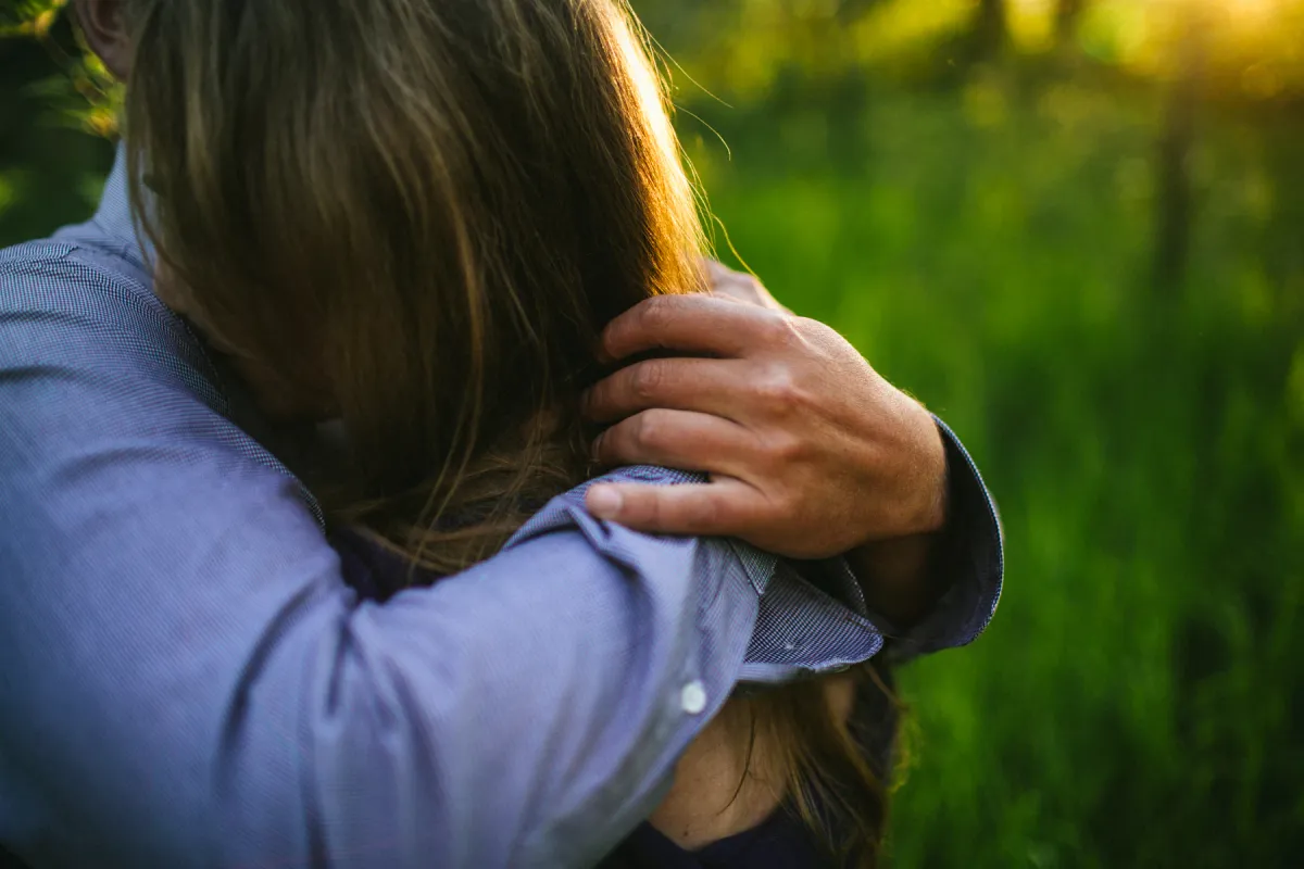 Close engagement photo of a hand resting on a partner shoulder in warm light