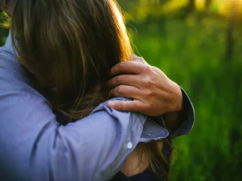 Close engagement photo of a hand resting on a partner shoulder in warm light