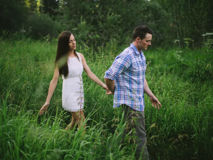 Couple walking hand in hand through tall green grass during an engagement session