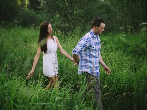 Couple walking hand in hand through tall green grass during an engagement session