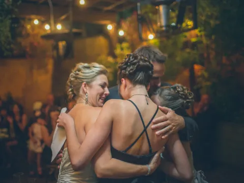 Bride and guests sharing a group hug outdoors at night under warm string lights
