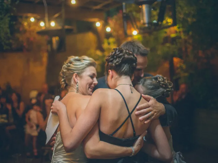 Bride and guests sharing a group hug outdoors at night under warm string lights